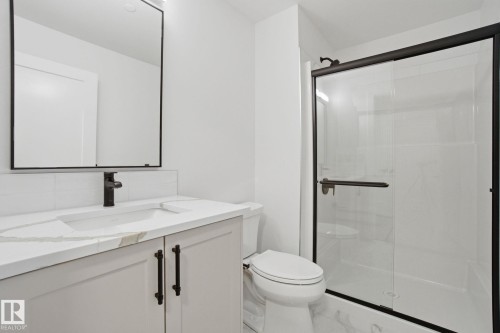 This bathroom features a contemporary vanity with a white countertop and dark hardware, a modern rectangular mirror, a toilet, and a glass-enclosed shower with dark framing - 516 260 Bellerose Dr, St. Albert, AB - Indoor Photo Showing Bathroom