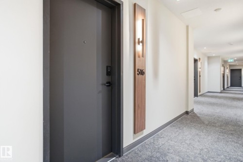 The property features a dark gray entrance door with a digital lock system, set within a well-lit hallway - 516 260 Bellerose Dr, St. Albert, AB - Indoor Photo Showing Other Room