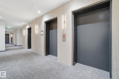 The property features a well-lit corridor with recessed lighting and modern wall sconces, textured wall finishes, and a patterned carpet - 516 260 Bellerose Dr, St. Albert, AB - Indoor Photo Showing Other Room
