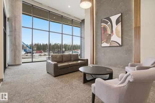 The property features expansive windows offering abundant natural light, a grey textured carpet, and a decorative accent wall with vertical wood paneling - 516 260 Bellerose Dr, St. Albert, AB - Indoor