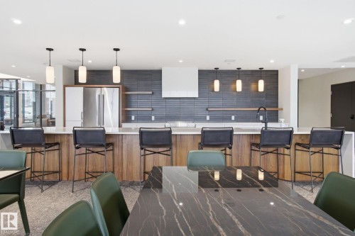 Kitchen area featuring a large island with white countertops and wooden paneling, a dark tiled backsplash, and stainless steel appliances - 516 260 Bellerose Dr, St. Albert, AB - Indoor