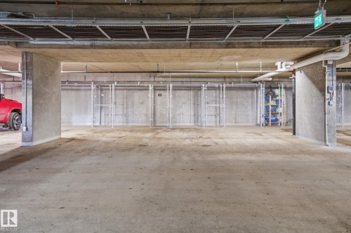 Concrete flooring within the property's parking area, featuring wire mesh storage lockers and exposed overhead utilities - 516 260 Bellerose Dr, St. Albert, AB - Indoor Photo Showing Garage