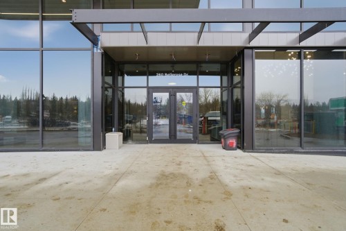 The property features a modern building exterior with large glass windows and doors, set on a concrete paved area - 516 260 Bellerose Dr, St. Albert, AB - Outdoor