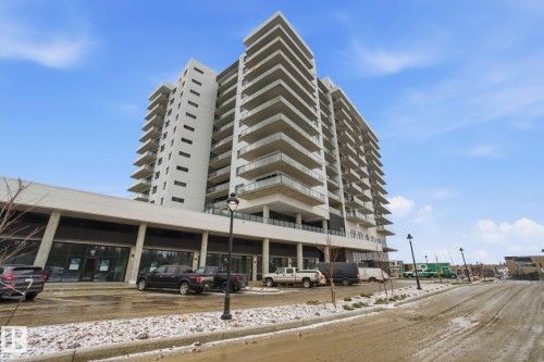 The property features a multi-story building with numerous balconies, and ground-level commercial spaces with large glass storefronts - 516 260 Bellerose Dr, St. Albert, AB - Outdoor With Balcony With Facade