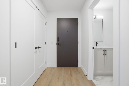 Entryway featuring light hardwood flooring and white walls, with a dark wood entry door equipped with modern hardware - 516 260 Bellerose Dr, St. Albert, AB - Indoor Photo Showing Other Room