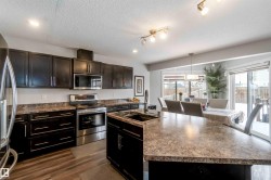 The kitchen features dark cabinetry, stainless steel appliances, and a large central island with a sink - 