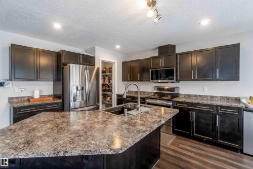 Kitchen featuring dark cabinetry, speckled countertops, stainless steel appliances, and a central island with an integrated sink - 12232 167B Avenue, Edmonton, AB - Indoor Photo Showing Kitchen With Stainless Steel Kitchen With Double Sink With Upgraded Kitchen