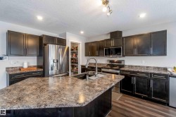 Kitchen featuring dark cabinetry, speckled countertops, stainless steel appliances, and a central island with an integrated sink - 