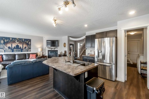 Open concept kitchen and living area featuring dark wood flooring, a central kitchen island with an undermount sink, dark kitchen cabinetry, and a stainless steel refrigerator - 12232 167B Avenue, Edmonton, AB - Indoor Photo Showing Kitchen With Stainless Steel Kitchen With Double Sink With Upgraded Kitchen