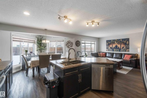 This open-concept living space features dark hardwood flooring, a kitchen island with a sink and dishwasher, and a dining area with large bay windows - 12232 167B Avenue, Edmonton, AB - Indoor Photo Showing Kitchen With Double Sink