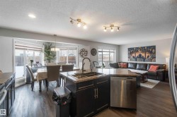 This open-concept living space features dark hardwood flooring, a kitchen island with a sink and dishwasher, and a dining area with large bay windows - 