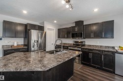 The kitchen features dark cabinetry, stainless steel appliances, and ample counter space with a large island - 