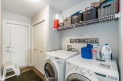 The laundry room features a washer and dryer, a white wire shelf, and a white door with a silver handle - 