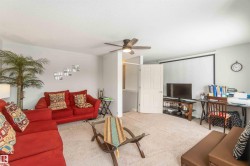 Spacious living area featuring light-colored carpeting, a ceiling fan, and a neutral wall color - 