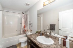 The bathroom features a white bathtub with a shower, a toilet, and a vanity with a large mirror and a single sink - 