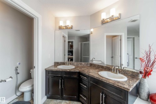 Bathroom featuring a double vanity with dark wood cabinetry, a light-colored countertop, and two mirrors with overhead lighting - 12232 167B Avenue, Edmonton, AB - Indoor Photo Showing Bathroom