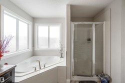 The bathroom features a built-in corner bathtub with a brushed nickel faucet and two windows, alongside a standing shower with a glass enclosure - 