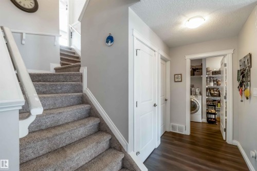 Inviting entryway featuring dark wood-style flooring, a staircase with carpeted treads and white banisters, and a laundry area with a washing machine and shelving - 12232 167B Avenue, Edmonton, AB - Indoor Photo Showing Other Room