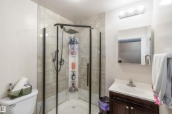 Bathroom featuring a glass-enclosed shower with a rainfall shower head, light-toned tiled walls, and a vanity with a white countertop - 