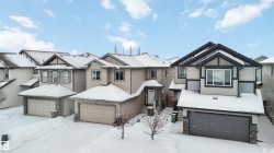 The property features a two-story exterior with light-colored siding, dark trim, and a prominent front-facing garage - 