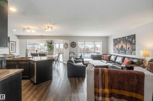 This property features an open-concept living space with dark wood flooring, a kitchen island with a sink, and a dining area with a glass sliding door leading to the exterior - 12232 167B Avenue, Edmonton, AB - Indoor Photo Showing Living Room