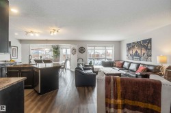 This property features an open-concept living space with dark wood flooring, a kitchen island with a sink, and a dining area with a glass sliding door leading to the exterior - 