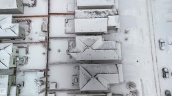 Aerial view showcasing properties with snow-covered roofs and yards, featuring a visible road with parked vehicles - 