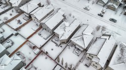 Aerial view of the neighborhood showcasing several properties with snow-covered roofs and yards, and a street with parked vehicles - 