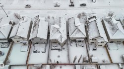 Aerial view of the property and surrounding neighborhood, featuring residential homes with pitched roofs, and a paved street with parked cars - 