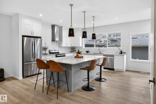 The kitchen features a spacious island with a light-colored countertop, stainless steel appliances, white cabinetry, and light-toned flooring - 6127 Carr Road, Edmonton, AB - Indoor Photo Showing Kitchen With Upgraded Kitchen