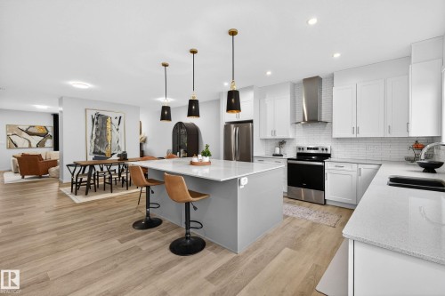 Modern kitchen featuring a large island with seating, white cabinetry, stainless steel appliances, and light-colored flooring - 6127 Carr Road, Edmonton, AB - Indoor Photo Showing Kitchen With Upgraded Kitchen