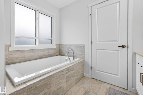 Soaking tub with tiled surround, accompanied by a window with frosted glass - 6127 Carr Road, Edmonton, AB - Indoor Photo Showing Bathroom