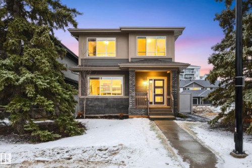 This property features a modern exterior with a mix of siding and brick detailing, illuminated windows, and a welcoming front entrance - 6127 Carr Road, Edmonton, AB - Outdoor With Facade