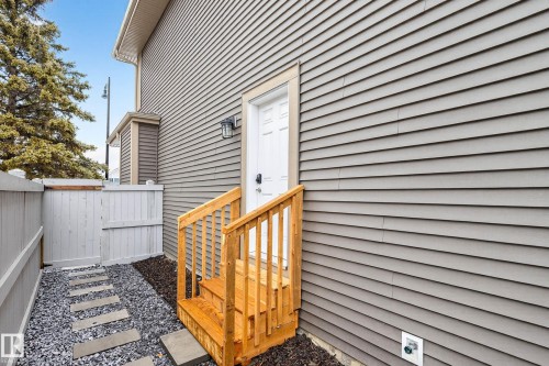 The property features gray siding, a white entry door with a wall-mounted light fixture, and wooden steps with railings - 6127 Carr Road, Edmonton, AB - Outdoor