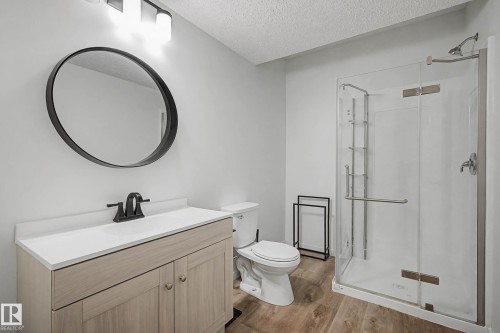 Bathroom featuring a light-toned wood vanity with a white countertop, a black framed circular mirror, and a clear glass shower enclosure - 6127 Carr Road, Edmonton, AB - Indoor Photo Showing Bathroom