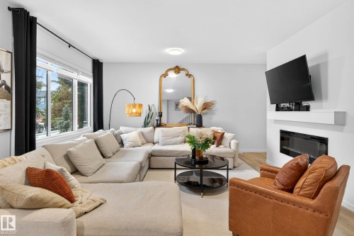 Spacious living area featuring large windows, a fireplace, and light-colored flooring - 6127 Carr Road, Edmonton, AB - Indoor Photo Showing Living Room With Fireplace