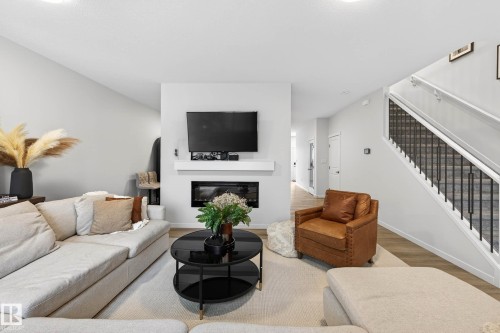 The living area features light-colored walls, a modern fireplace, and wood flooring - 6127 Carr Road, Edmonton, AB - Indoor Photo Showing Living Room With Fireplace