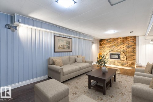 Living area featuring light blue paneled walls, dark wood flooring, and a brick fireplace - 7324 77 Street, Edmonton, AB - Indoor Photo Showing Living Room With Fireplace