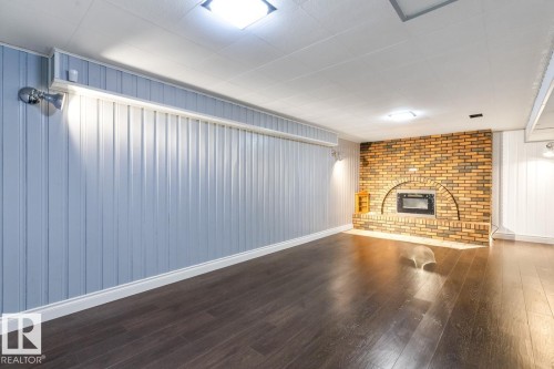 This property features rich, dark wood flooring, a decorative brick fireplace with an arched opening, and light blue paneling on the walls - 7324 77 Street, Edmonton, AB - Indoor Photo Showing Living Room With Fireplace