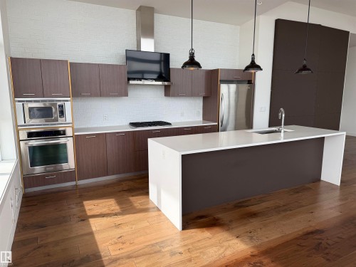 The kitchen features hardwood floors, a large island with a sink, stainless steel appliances, and white subway tile backsplash - 710 2504 109 Street, Edmonton, AB - Indoor Photo Showing Kitchen With Upgraded Kitchen