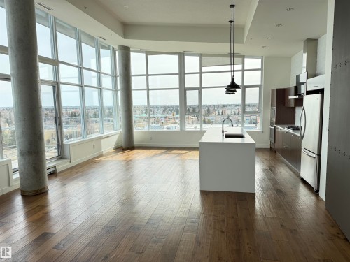 Contemporary open-concept living space featuring expansive windows, hardwood flooring, a modern kitchen island with an integrated sink, and stainless steel appliances - 710 2504 109 Street, Edmonton, AB - Indoor Photo Showing Other Room