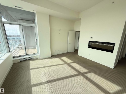 Living area featuring carpeted floors, an integrated wall fireplace, and a large sliding glass door leading to an outdoor space - 710 2504 109 Street, Edmonton, AB - Indoor With Fireplace