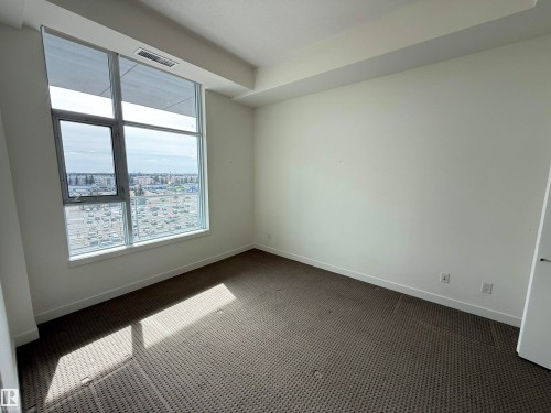 This room features large windows providing a panoramic view of the surrounding cityscape, light-colored walls, and a textured carpeted floor - 710 2504 109 Street, Edmonton, AB - Indoor Photo Showing Other Room