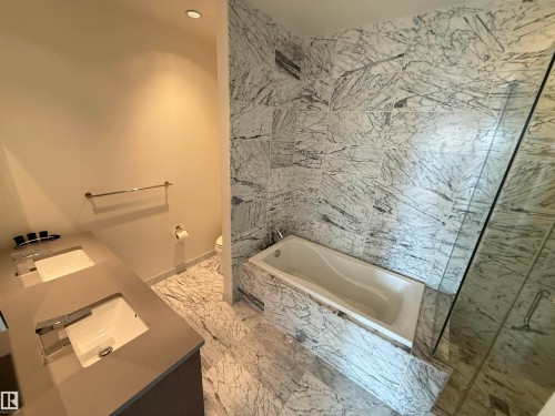 Well-appointed bathroom featuring a double vanity with integrated sinks, polished chrome fixtures, and extensive marble tiling throughout the floors and shower surround - 710 2504 109 Street, Edmonton, AB - Indoor Photo Showing Bathroom