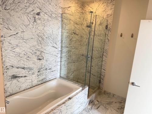 Bathroom featuring a built-in bathtub, a walk-in shower with clear glass enclosure, and walls and flooring adorned with marble-patterned tiles - 710 2504 109 Street, Edmonton, AB - Indoor Photo Showing Bathroom