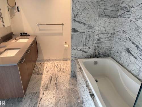 A luxurious bathroom featuring a double vanity with ample storage, a deep soaking tub, and elegant marble floor and wall tiling - 710 2504 109 Street, Edmonton, AB - Indoor Photo Showing Bathroom