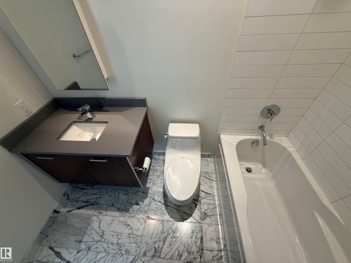 The bathroom features a modern vanity with a dark countertop and integrated sink, a white bathtub, and white tile walls in the shower area - 710 2504 109 Street, Edmonton, AB - Indoor Photo Showing Bathroom