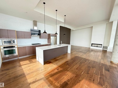 Open concept living space featuring wide plank wood flooring, a contemporary kitchen with stainless steel appliances, a kitchen island with a sink, and a modern fireplace - 710 2504 109 Street, Edmonton, AB - Indoor Photo Showing Kitchen With Upgraded Kitchen
