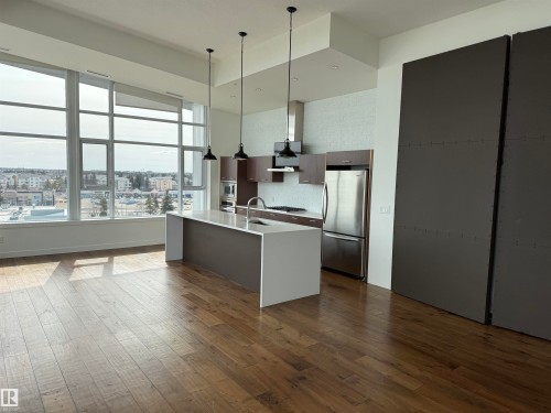 The property features expansive windows offering urban views, hardwood flooring, and a modern kitchen with an island, stainless steel appliances, and pendant lighting - 710 2504 109 Street, Edmonton, AB - Indoor Photo Showing Kitchen