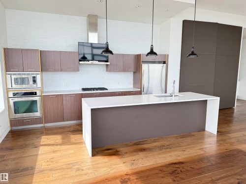 The kitchen features hardwood floors, a central island with a sink, stainless steel appliances, and pendant lighting - 710 2504 109 Street, Edmonton, AB - Indoor Photo Showing Kitchen With Upgraded Kitchen